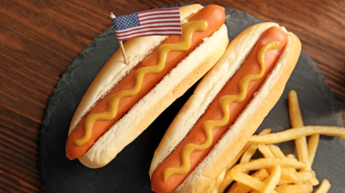Hot,Dogs,With,Mustard,And,Small,Usa,Flag,On,Slate